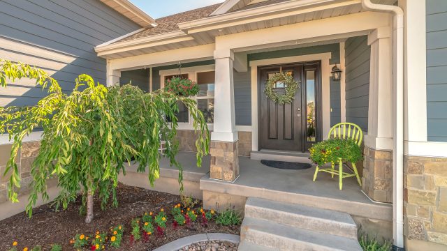 blue siding, black door, stone accent, front porch, hanging basket, landscaping, outdoor decor, green chair, flower bed