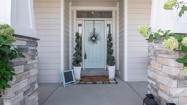 light blue door, stone columns, neutral siding, front entryway, wreath decor, potted plants, plaid doormat, classic exterior design